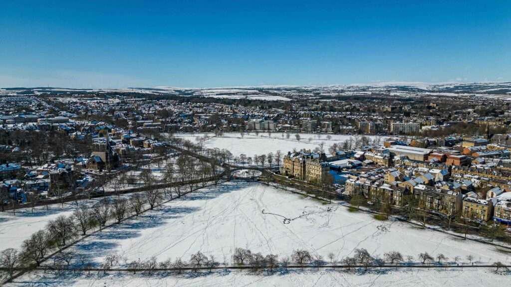 Vue aérienne hivernale d'une ville enneigée avec des bâtiments et des arbres nus, sous un ciel bleu clair à Harrogate, dans le Yorkshire du Nord.