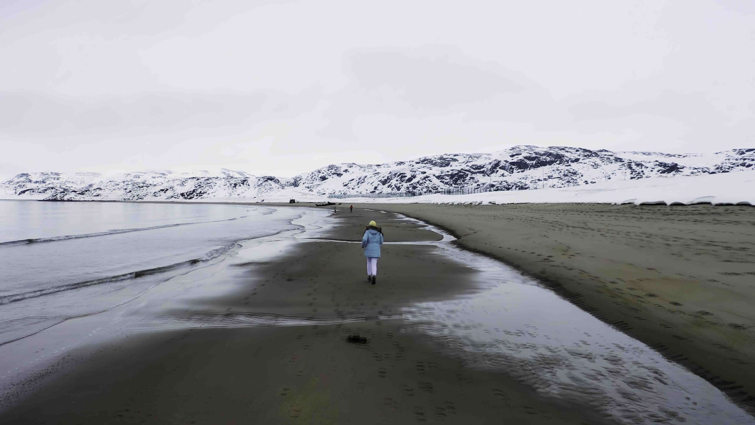 Paysage à couper le souffle avec une côte de mer hivernale entourée de collines enneigées sur fond de ciel lumineux. Images. Vue arrière d'une fille courant le long de la côte froide de la mer.